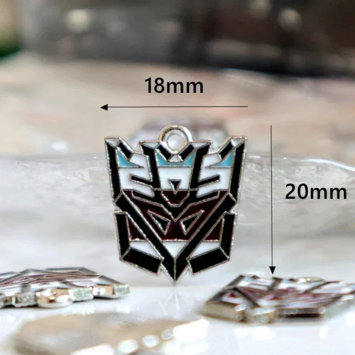 Pendentif émail tête Decepticon noir, blanc et bleu, 18mm x 20mm, posé sur surface claire – Transformers.