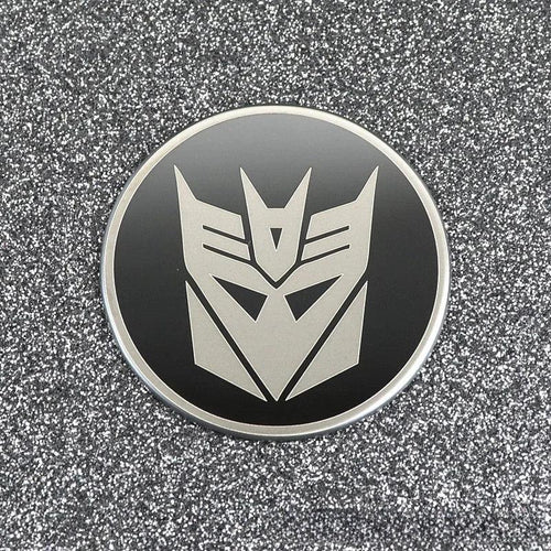 Badge rond noir avec logo Decepticon argenté sur fond pailleté – Transformers.