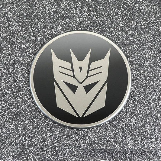 Badge rond noir avec logo Decepticon argenté sur fond pailleté – Transformers.