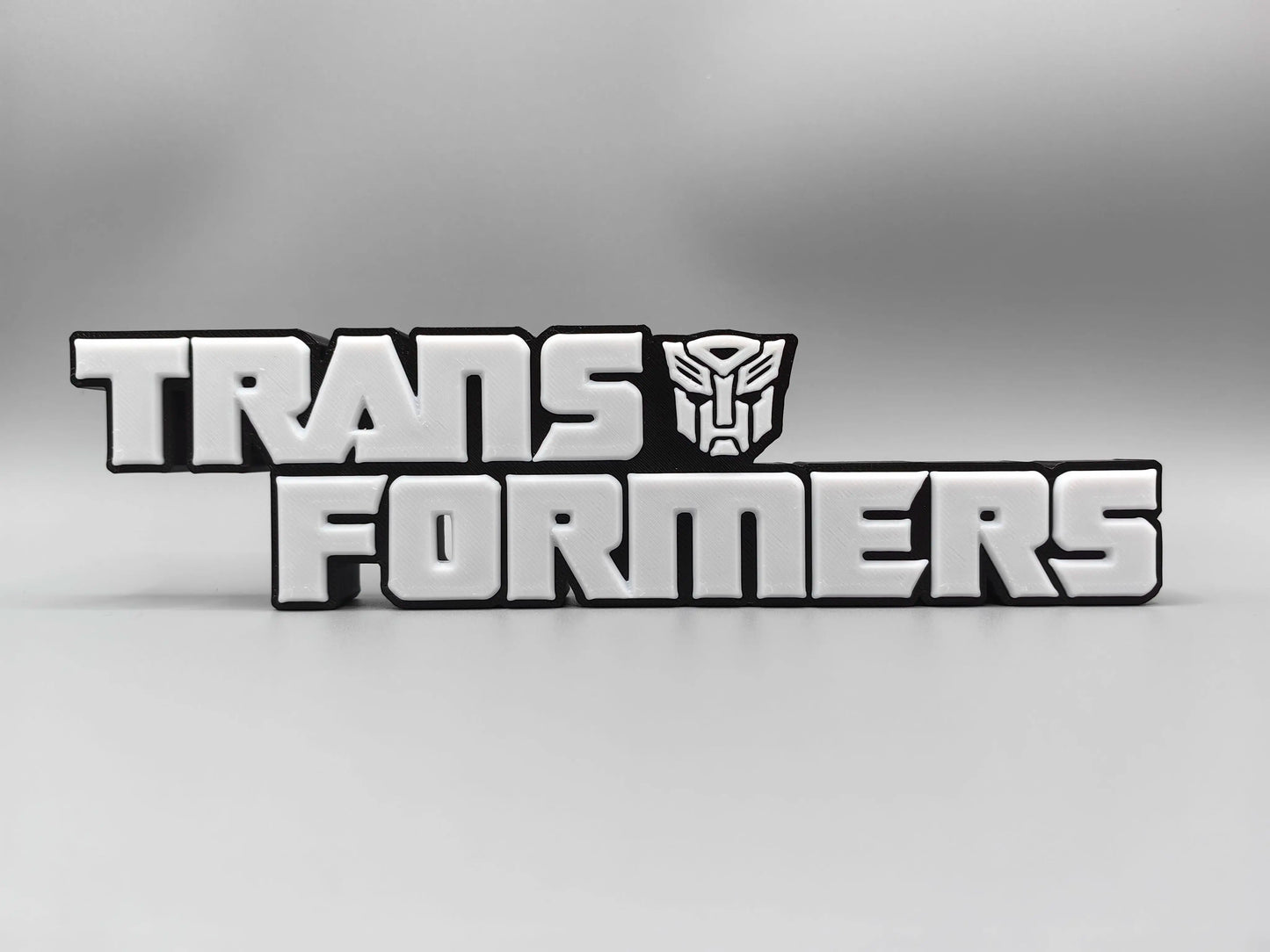 Tabliczka Transformers z monochromatycznym srebrnym logo — Metalizowana dekoracja na biurko